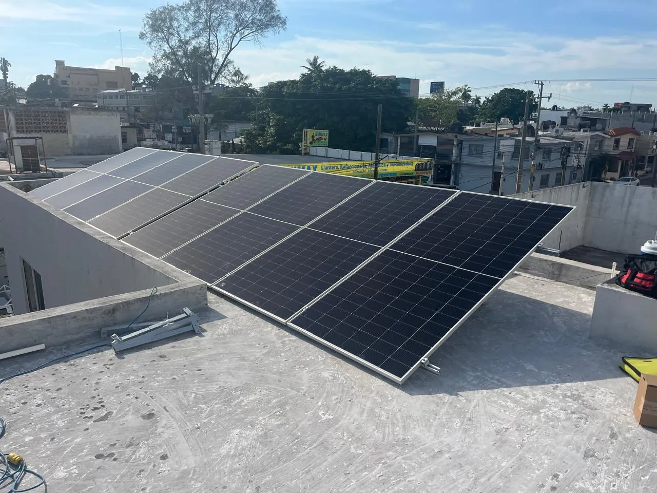 Sistema solar instalado en un techo de concreto en zona urbana, con negocios locales de fondo